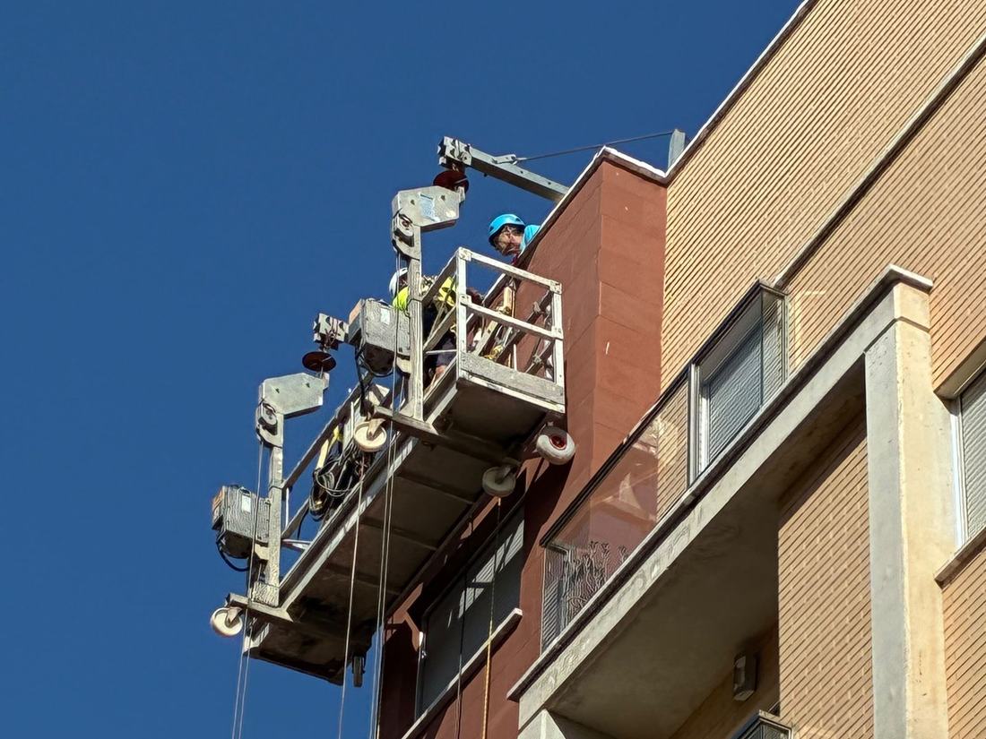 Operarios trabajando sobre una plataforma suspendida en la fachada de un edificio